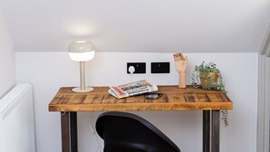 A workspace with a wooden desk, a black office chair, a desk lamp, a newspaper, and a small plant. - Settle Southampton (Southampton)