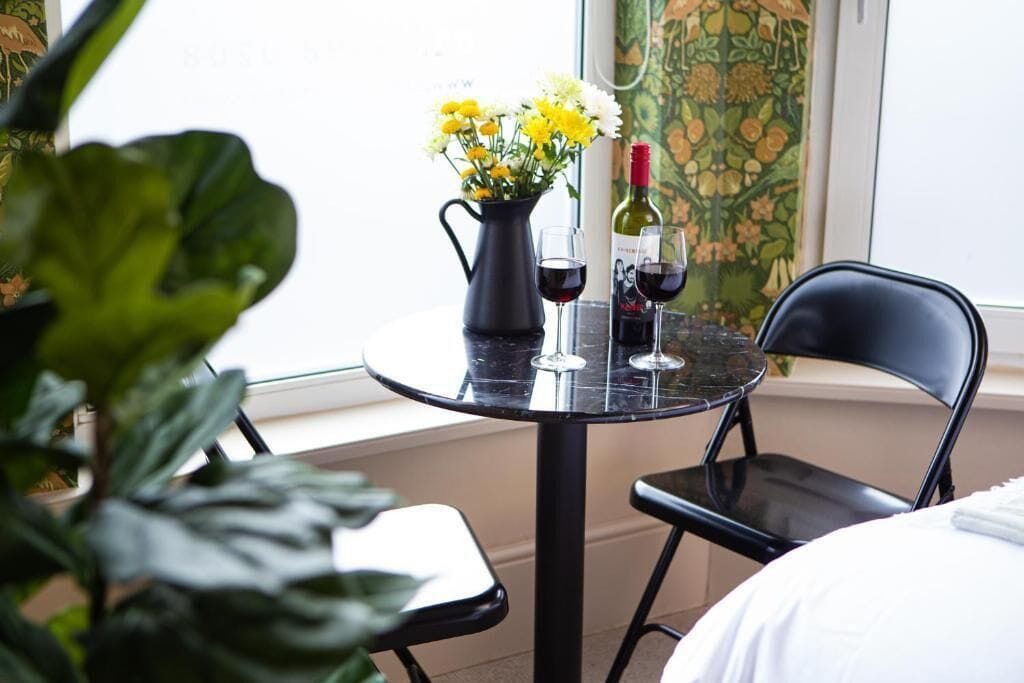 A room with a round table, two chairs, a vase with flowers, and two wine glasses.