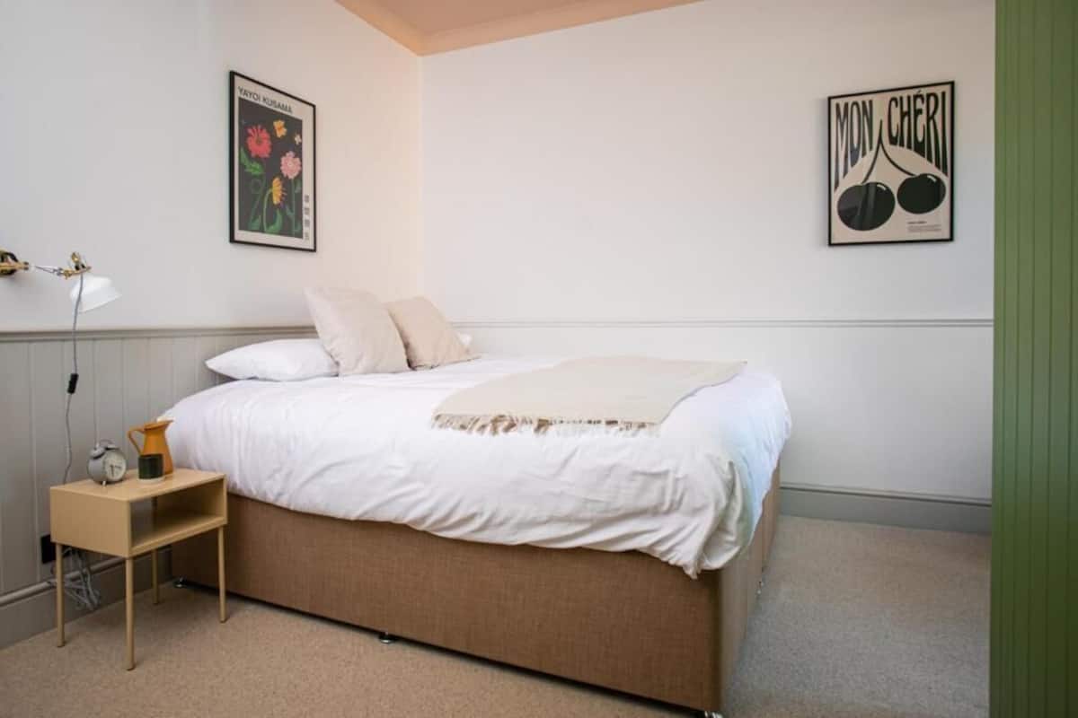 A bedroom with a bed, a bedside table with a lamp, and two framed pictures on the wall.
