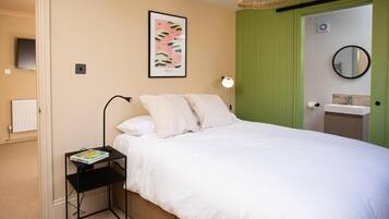 Un dormitorio con cama, una mesita de noche con un libro, una lámpara de pared, un cuadro enmarco, una puerta verde y un espejo redondo.