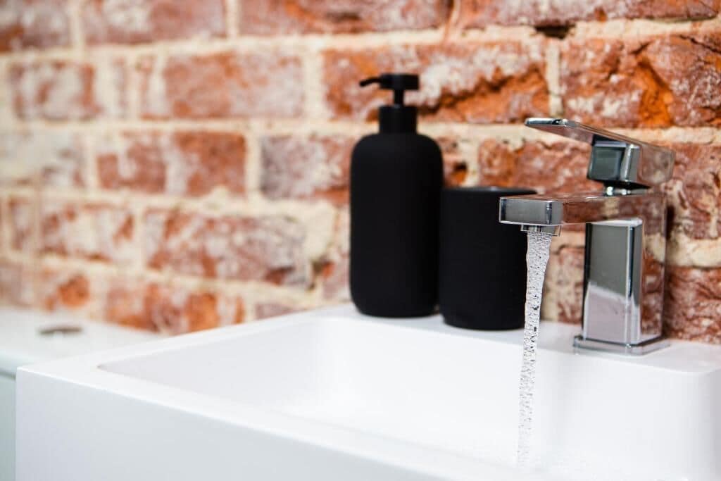 A bathroom with a white sink, a chrome faucet, and a black soap dispenser.