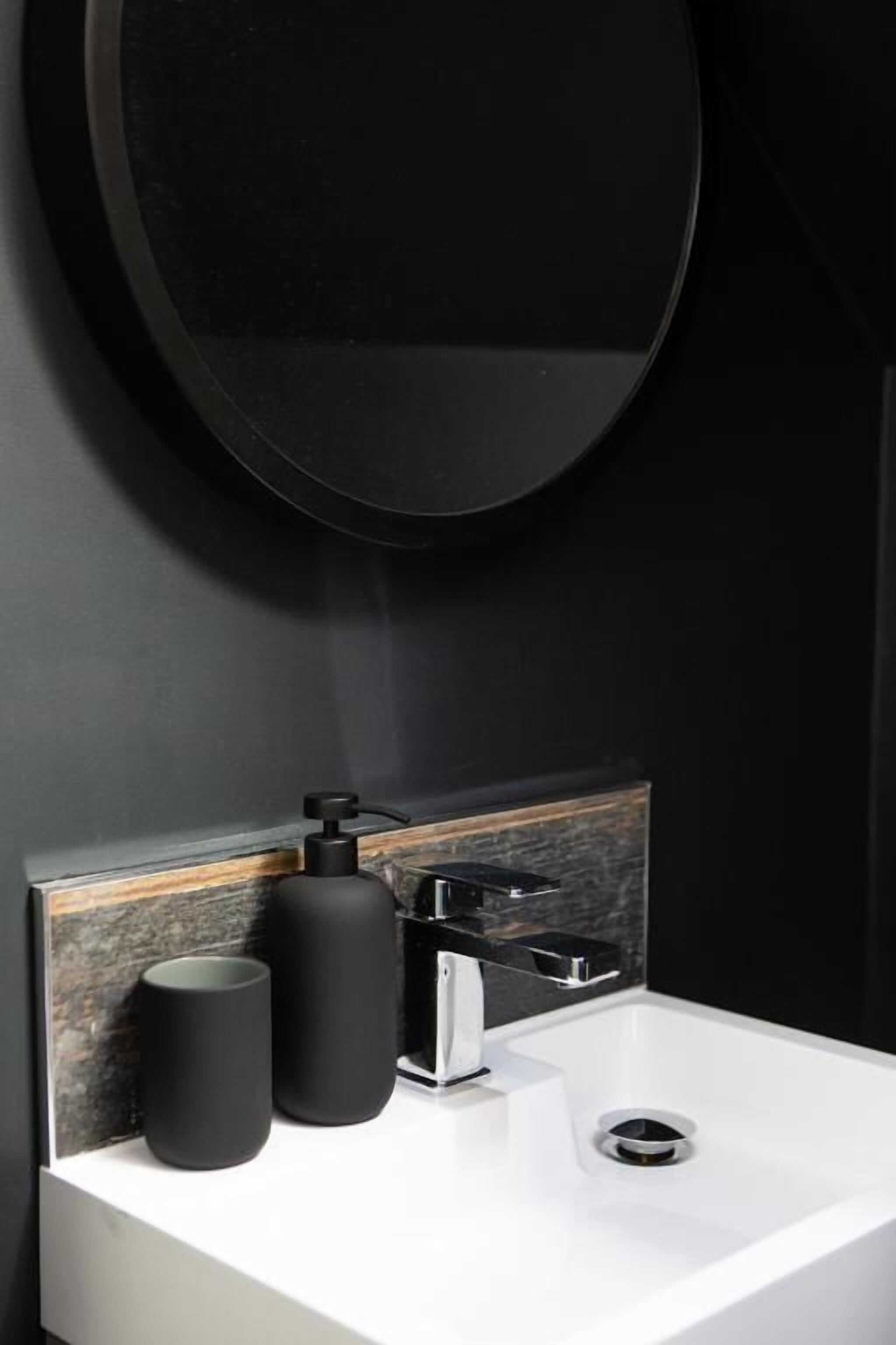 A modern bathroom with a white sink, black soap dispensers, and a round mirror.