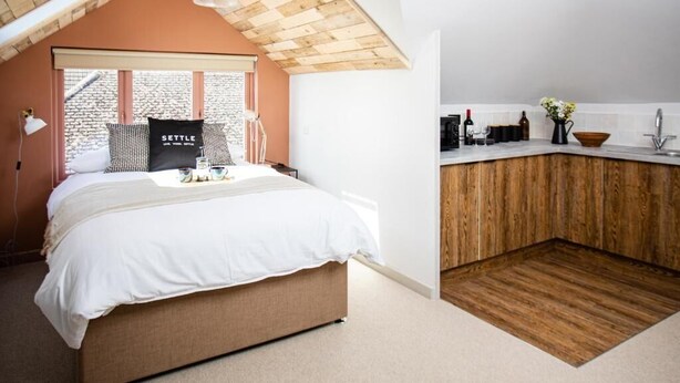 A bedroom with a large bed, a wooden ceiling, and a view of a brick building outside. - Settle Southampton (Southampton)
