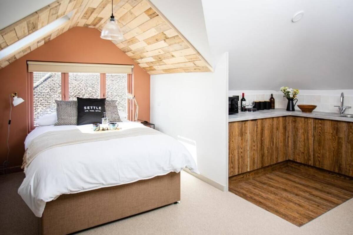 A bedroom with a large bed, a wooden ceiling, and a view of a brick building outside.