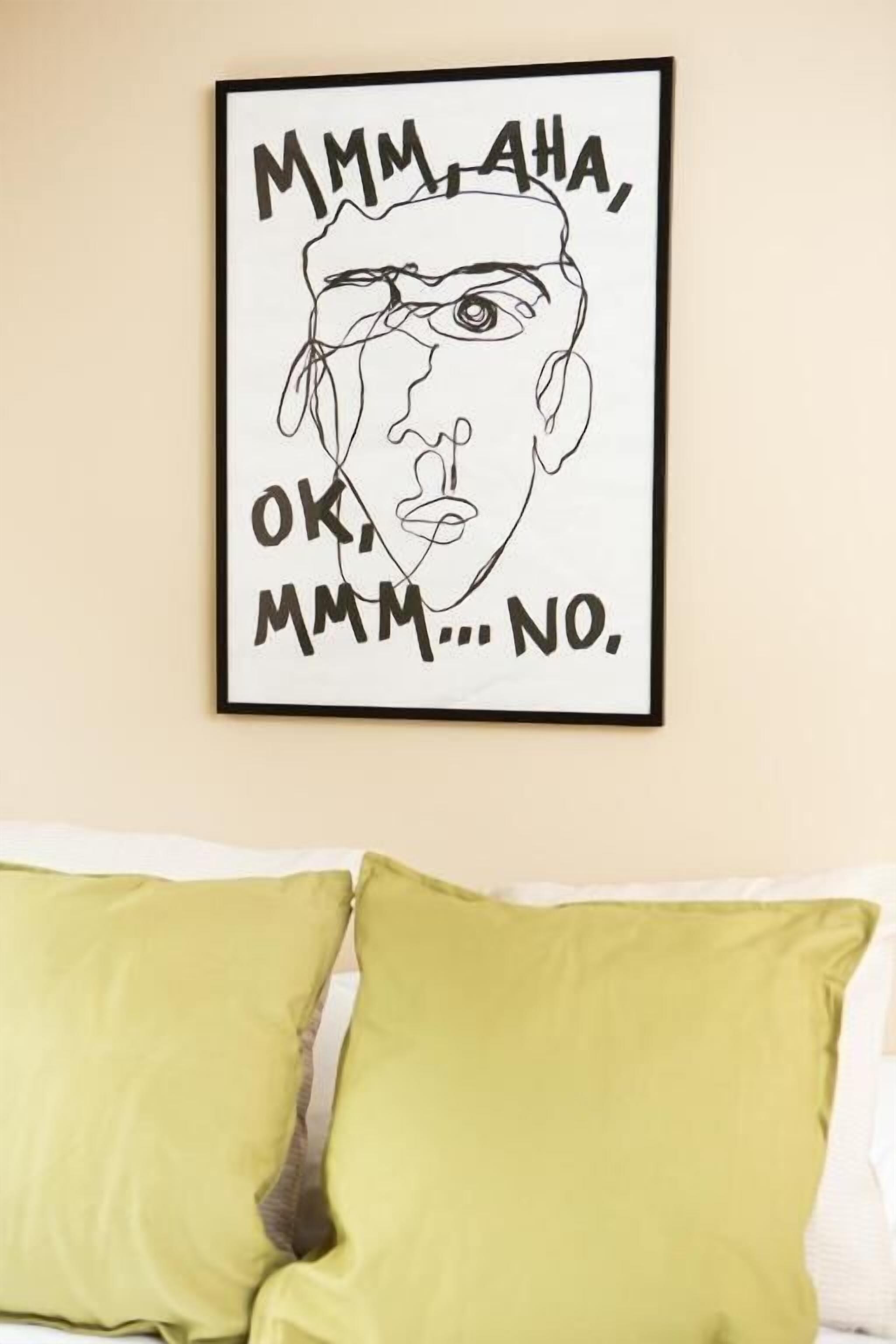 Una obra de arte enmarco con texto en una pared, una cama con almohadas verdes y una pared lisa.