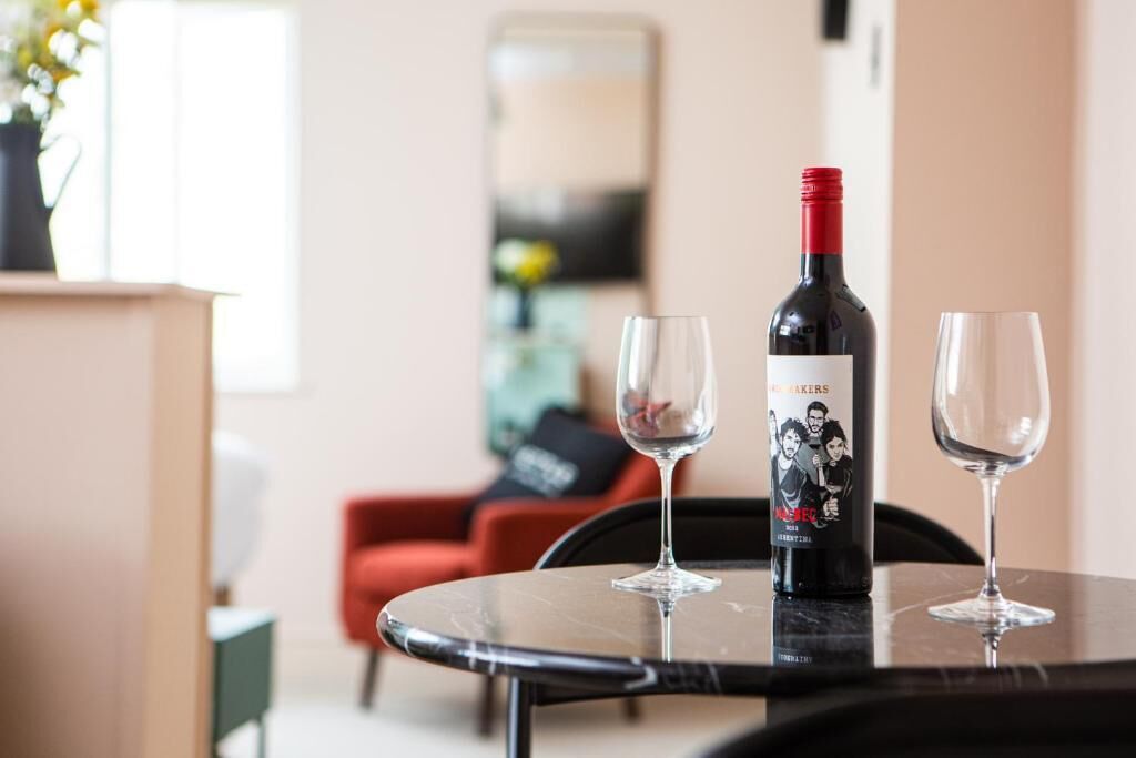 Ein Tisch mit einer Weinflasche und zwei Gläsern, ein roter Stuhl und ein modernes Interieur.