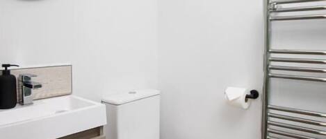 Un bany amb un rentapans blanc, un mirall, un vàter i una barra de tovalloles.