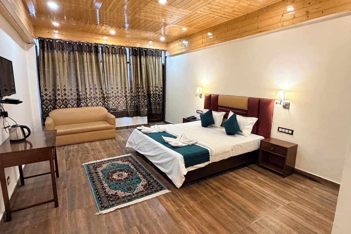 A bedroom with a wooden ceiling, a bed with a headboard, a bedside table, a sofa, and a patterned rug.