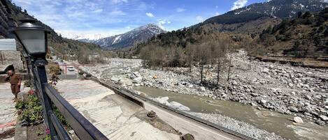 A river with a bridge, mountains in the background, and a person walking on the bridge.