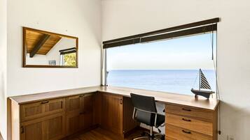 A corner desk with a view of the sea, a small sailboat model, and a mirror on the wall.