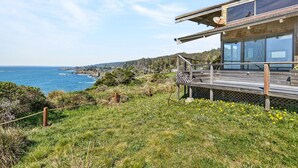 Una propiedad costera con terraza con vistas al mar, cerca de una valla de madera y con una vista despejada del océano.
