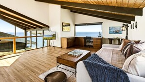 Un interior moderno con un ventanal grande, vigas de madera en el techo, un sofá, una mesa de centro y una zona de escritorio.