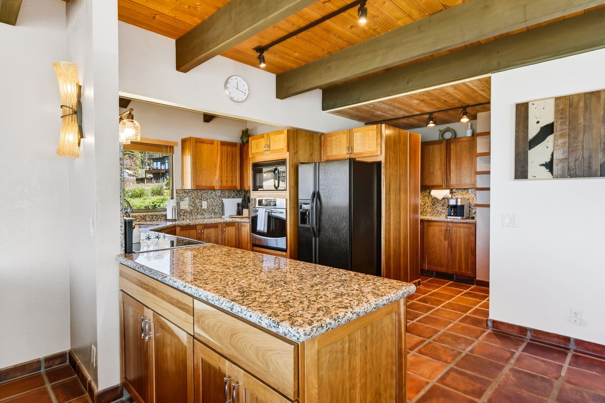 A kitchen with wooden cabinets, granite countertops, a black refrigerator, and a clock on the wall.