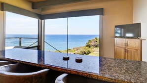 Una cocina moderna con un amplio ventanal con vistas al océano, techo de madera y televisor de pantalla plana sobre un mueble.