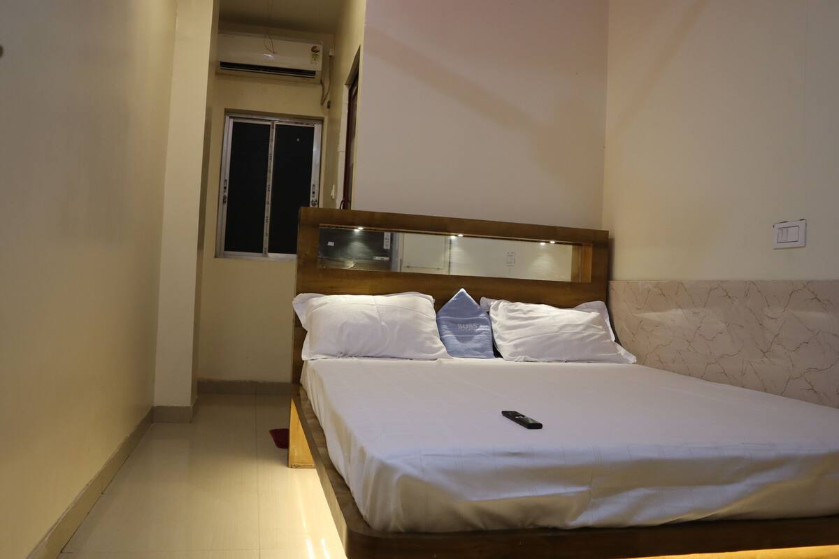 A hotel room with a bed, a bedside table, a mirror, and a window.