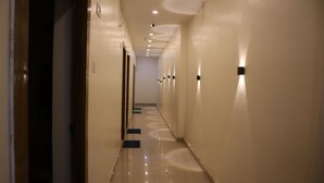 Un pasillo de hotel largo, con puertas a la izquierda y luces en la pared a la derecha.