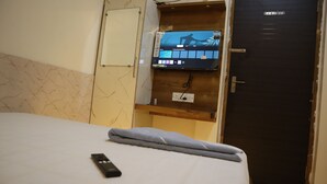 Habitación de hotel con cama, control remoto, televisor montado en un panel de madera y una puerta.