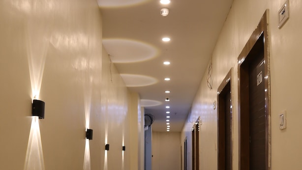 Un pasillo de hotel con iluminación empotrada, un felpudo y puertas indicadas con números de habitación.