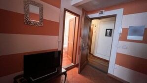 Un pasillo con un televisor sobre un mueble bajo, una puerta que da al baño y un interruptor de luz en la pared.