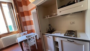 Cocina con estufa, lavamanos y alacenas. Hay una ventana con cortinas y un radiador.