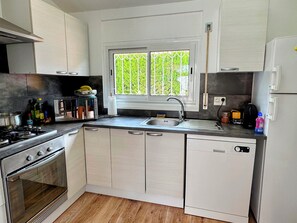 Eine kompakte Küche mit Gaskochfeld, Backofen, Spüle und einem Fenster mit Blick auf Grünflächen.