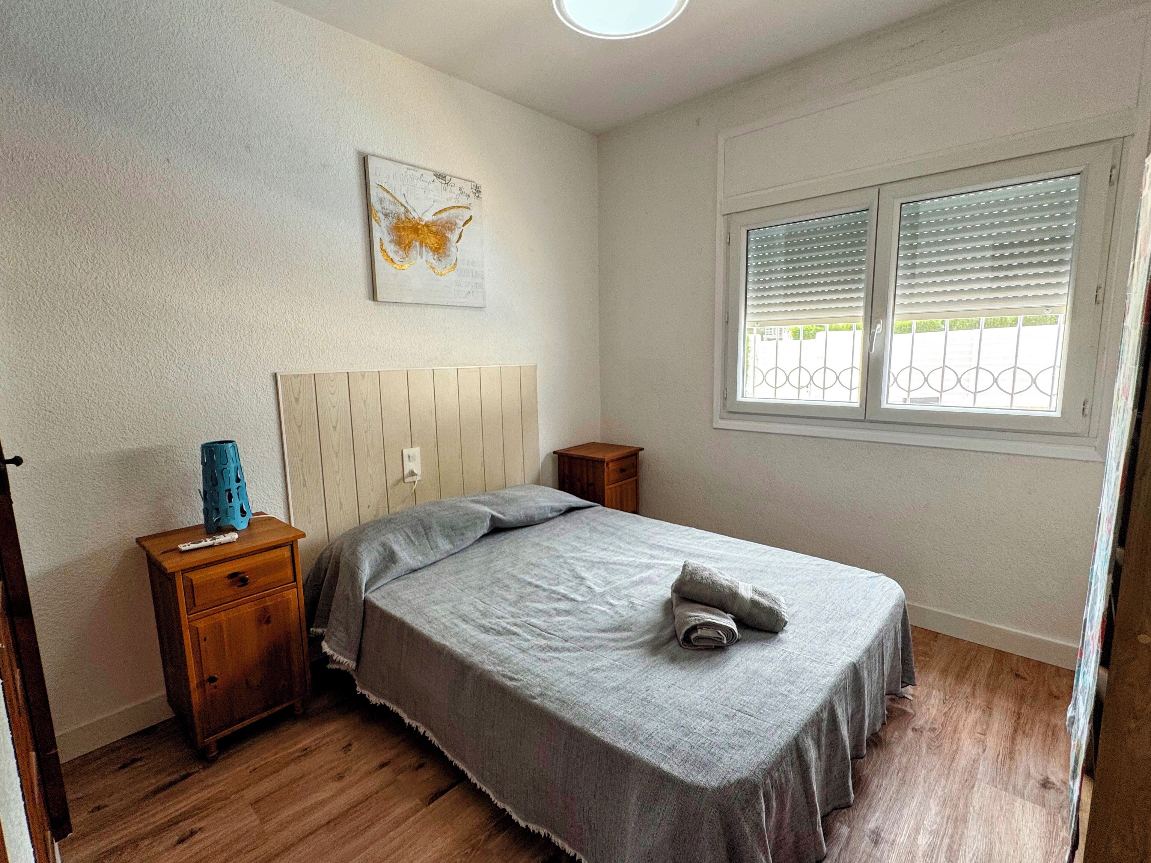 Quarto com cama, mesa de cabeceira, cortinas na janela e uma obra de arte na parede.