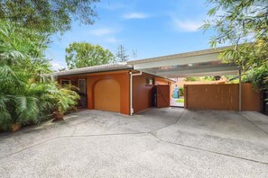 A garage with a covered carport, a closed garage door, and a concrete driveway. - Fuller Holidays -Villa Pomplamoose, Byron Town Centre (Byron)