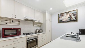 Uma cozinha moderna com armários brancos, um micro-ondas vermelho, fogão a gás e uma pia.