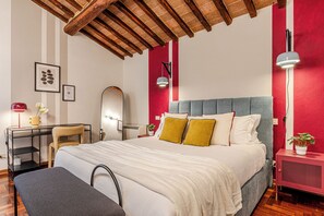 A bedroom with a bed, bedside table, desk, chair, and a red accent wall. - Sosta Eroica - Pool & Breathtaking Views over Siena (Asciano)