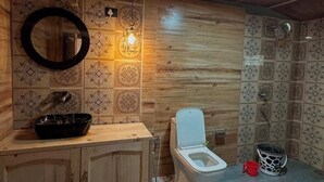Een badkamer met een houten wastafel, toilet, patroon betegelde vloer en een ronde spiegel.