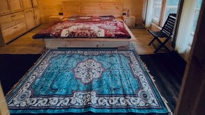 Een houten cabin met een bed, een vloerkleed, een stoel en een kleine tafel.