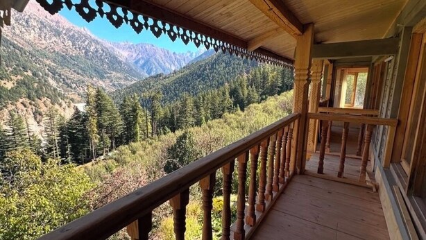 Een houten balkon met een hekwerk, met uitzicht op een bergachtig landschap.