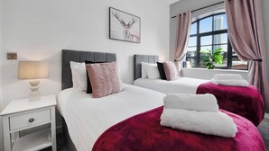 Una camera d'albergo con due letti, un comodino, una lampada, una finestra con tende e vista sulla città.