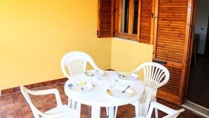 A small dining area with a round table and white plastic chairs, a window with wooden shutters, and a yellow wall. - Apartment with balcony and parking space (Numana)