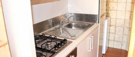 A compact kitchen with a gas stove, stainless steel sink, and white cabinets.