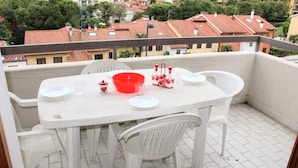 A balcony with a white table and chairs, a red bowl, and a view of red-tiled buildings.