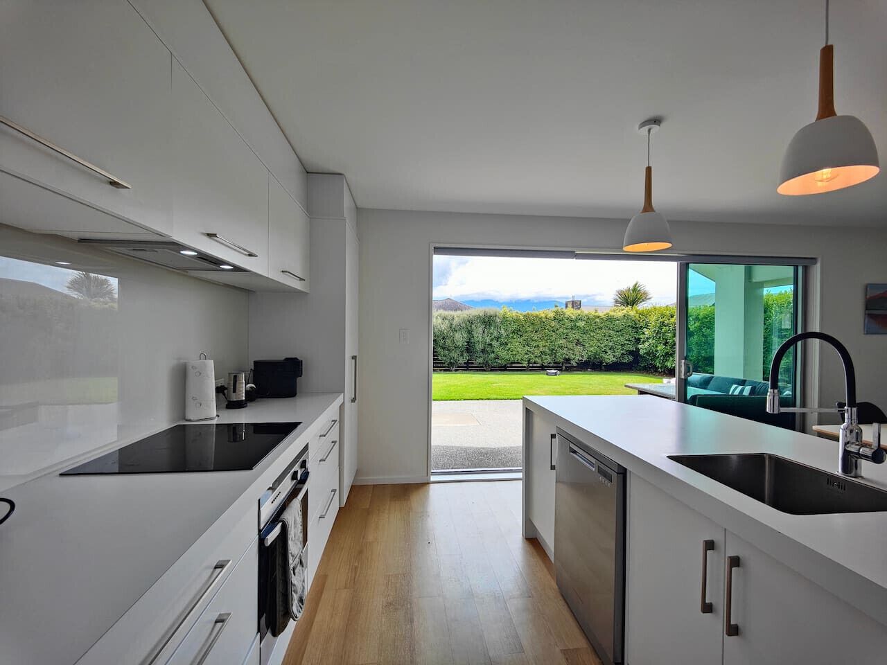 Une cuisine moderne avec des meubles blancs, une plaque de cuisson à induction noire et une grande fenêtre donnant sur un paysage verdoyant.