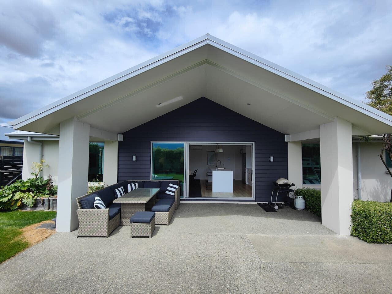 Uma casa moderna com varanda coberta, mobiliário de exterior e porta de vidro deslizante que dá para o interior.