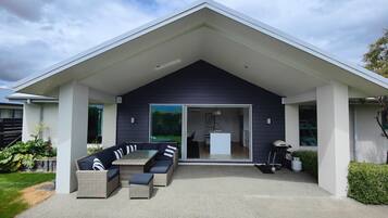Uma casa moderna com varanda coberta, mobiliário de exterior e porta de vidro deslizante que dá para o interior.