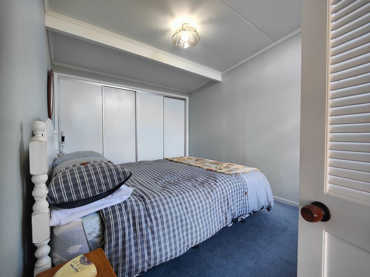A bedroom with a bed, a wardrobe, a door, and a ceiling light fixture.
