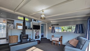A cozy living area with a sofa, a table with books, a fireplace, and a television. - Blue Bach in the Loop (Te Anau)