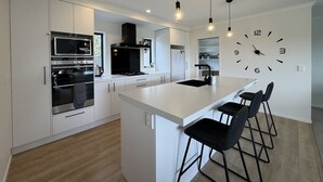 Une cuisine moderne avec des meubles blancs, un îlot central, des tabourets de bar noirs et une horloge murale.