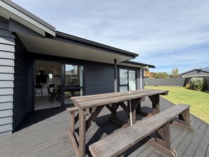 A wooden deck with a picnic table, a glass door entrance to a building, and a grassy yard.