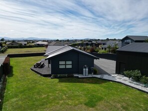 A modern house with a dark exterior, a well-maintained lawn, and a small deck with seating.