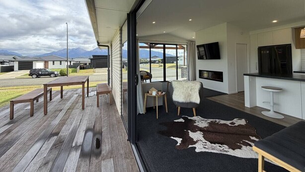 A modern interior with a wooden deck, a seating area with a fur throw, and a kitchen with a bar.
