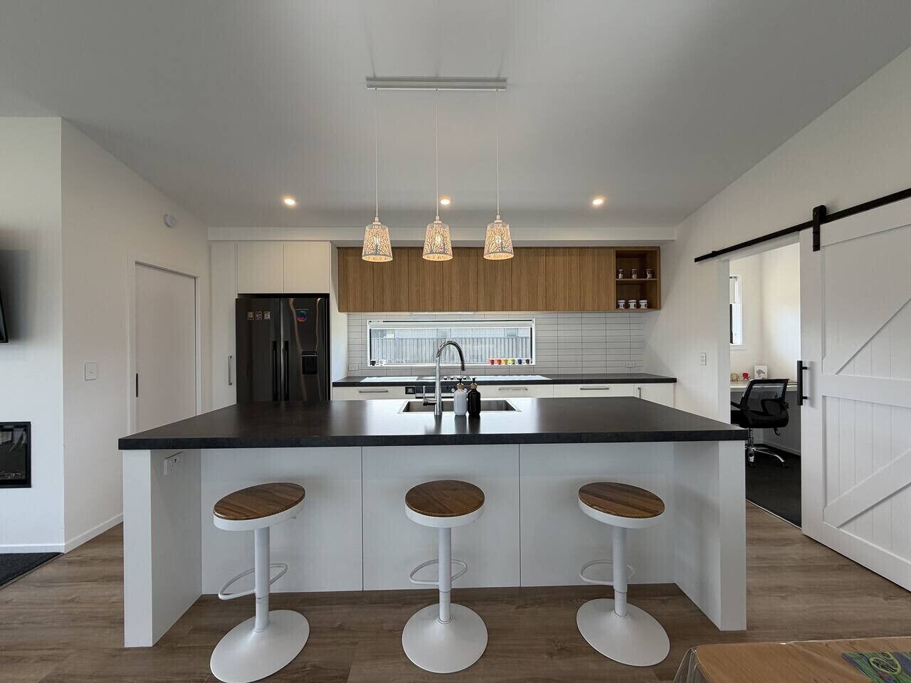 Una cocina moderna con una isla central, taburetes de bar, lámparas colgantes y un refrigerador.