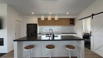 Una cocina moderna con una isla central, taburetes de bar, lámparas colgantes y un refrigerador.