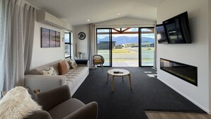A modern living room with a sofa, a coffee table, a fireplace, and a large window with a mountain view.