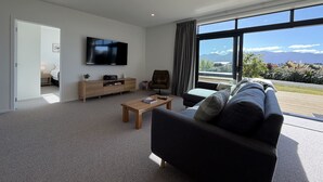 A modern living room with a large TV, a sofa, a coffee table, and a view of the outdoors.