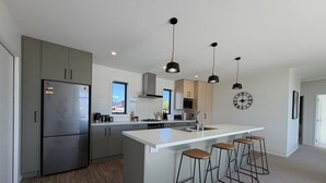 A modern kitchen with a central island, bar stools, pendant lights, and a clock on the wall.